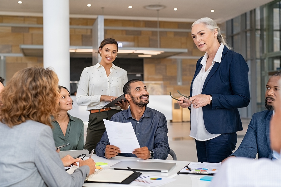 Group of business people discussing work in conference room. Senior business manager guiding employees in meeting. Group of businessman and businesswoman working together while sharing new strategy.
